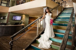 A staircase with a wooden handrail and teal steps, leading to a reception area with a desk and a monitor.