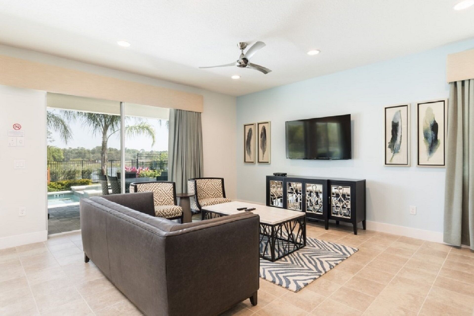 A modern living room with a grey sofa, patterned chairs, a coffee table, and a TV mounted on the wall.