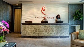 A reception desk with a logo and the name "ENCOFFI CLUB" above it. There are two individuals seated behind the desk, one using a laptop and the other working on a computer. - Free Shuttle,Official Encore Water Park,XBOX,Movie,Games,Cage,Pool/Spa,Star Wars (Kissimmee)