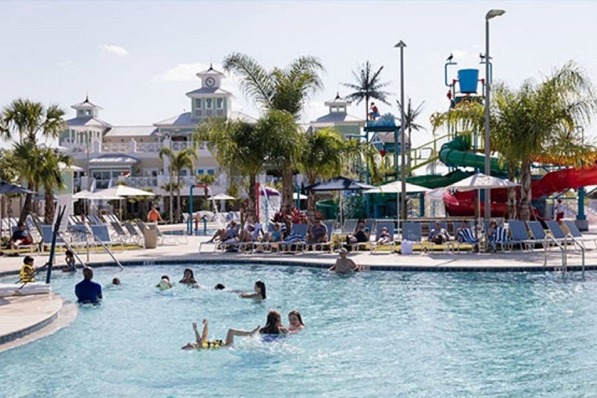 A swimming pool area with lounge chairs, palm trees, and a water slide.