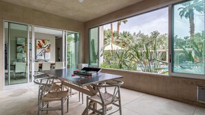 A modern dining area with a large table and chairs, large windows with a view of palm trees and a pool, and a ceiling fan. - Secluded 1-Acre Mountain View Retreat - great location in La Quinta  #112390 6BR (La Quinta)