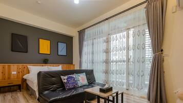 Ein modernes Zimmer mit einem Bett, einer Couch, einem kleinen Tisch und einem Fenster mit Vorhängen.
