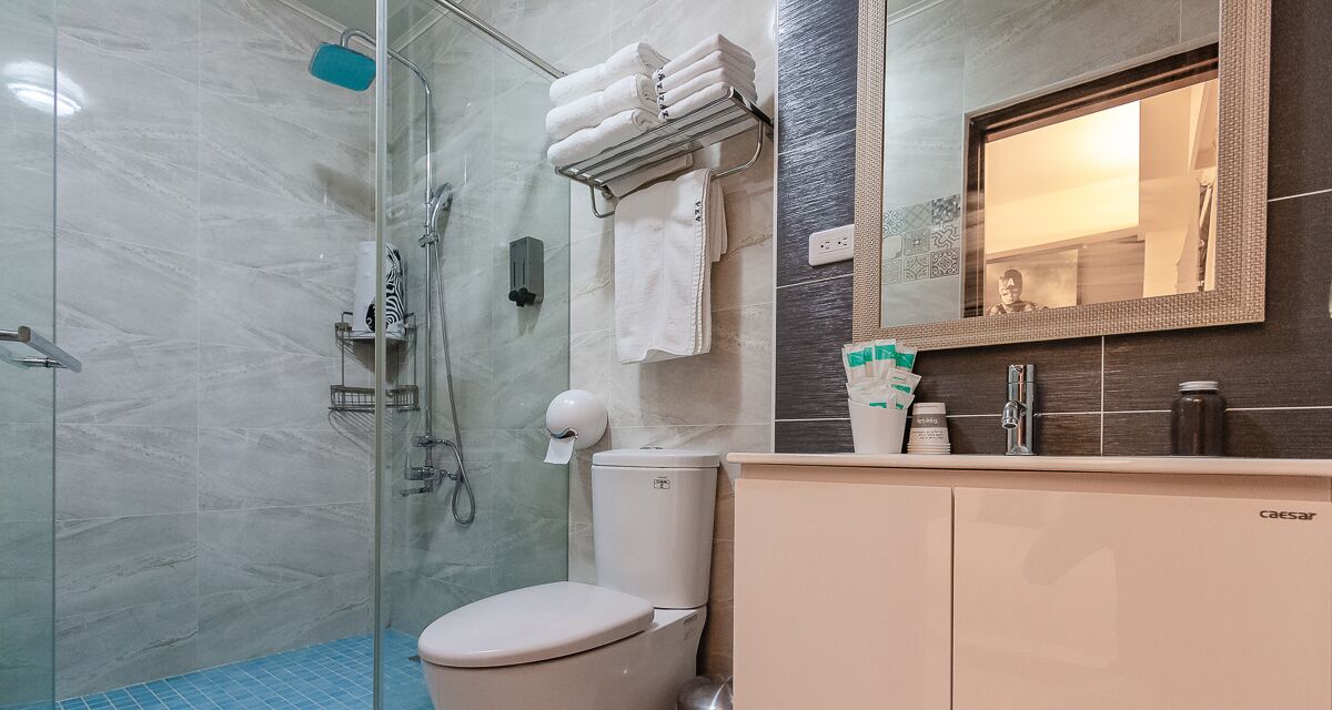 A modern bathroom with a glass shower enclosure, a toilet, a vanity with a mirror, and neatly folded towels on a rack.