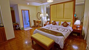 Una habitación de hotel con una cama grande, suelo de madera, un banco, un escritorio y un espejo.
