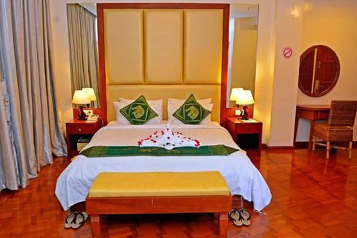 A hotel room with a large bed, two bedside tables with lamps, a wooden bench, a chair, and a mirror on the wall.