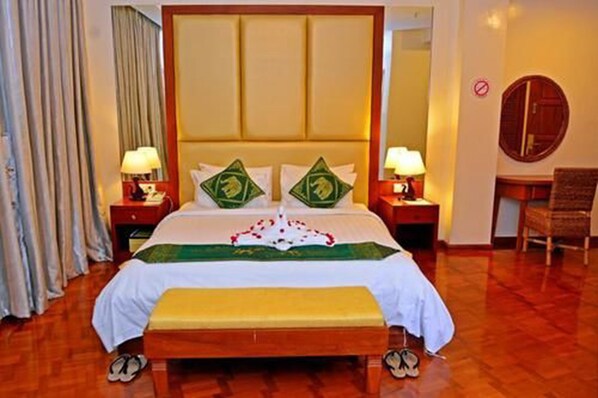 A hotel room with a large bed, two bedside tables with lamps, a wooden bench, a chair, and a mirror on the wall.