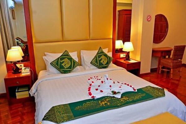 Una habitación de hotel con cama, dos mesitas de noche, una silla y un espejo.