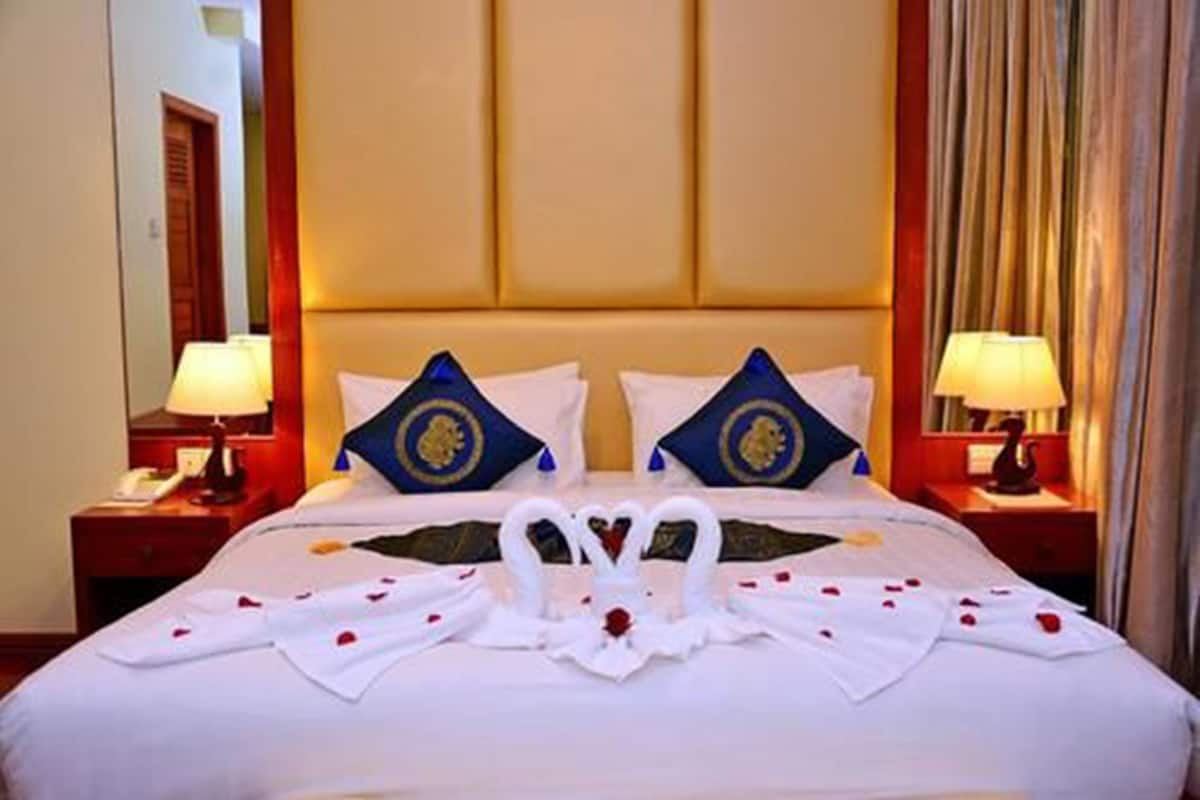 A hotel room with a large bed, two decorative pillows, a nightstand with a lamp, and a mirror.