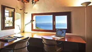 A workspace with a laptop, two wicker chairs, a desk, and a view of the sea through a large window. - PELION HOMES | Villa SELINI large traditional villa w/ pool & breathtaking view (Agios Georgios Nilias)