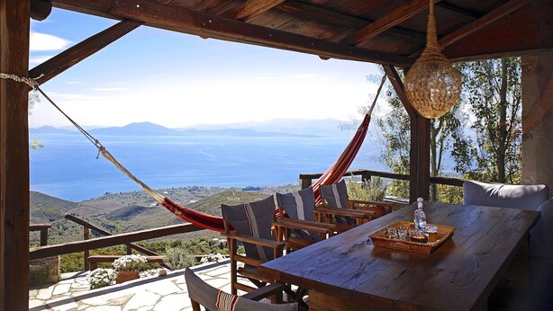 A wooden table with chairs and a hammock, overlooking a scenic view of hills and a body of water. - PELION HOMES | Villa SELINI large traditional villa w/ pool & breathtaking view (Agios Georgios Nilias)
