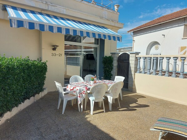 Eine Außenpatio mit Tisch und Stühlen, einem blau gestreiften Markisenstoff und einem Tor.