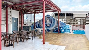 Un área de estar al aire libre con mesas y sillas, un mural con diseño de tigre y vistas a edificios al fondo.