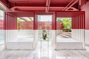 Un espace int érieur moderne aux couleurs rouge et blanche, avec un sol en marbre, une table centrale agrémentée d’un vase et une vue sur un escalier menant à l’extérieur.