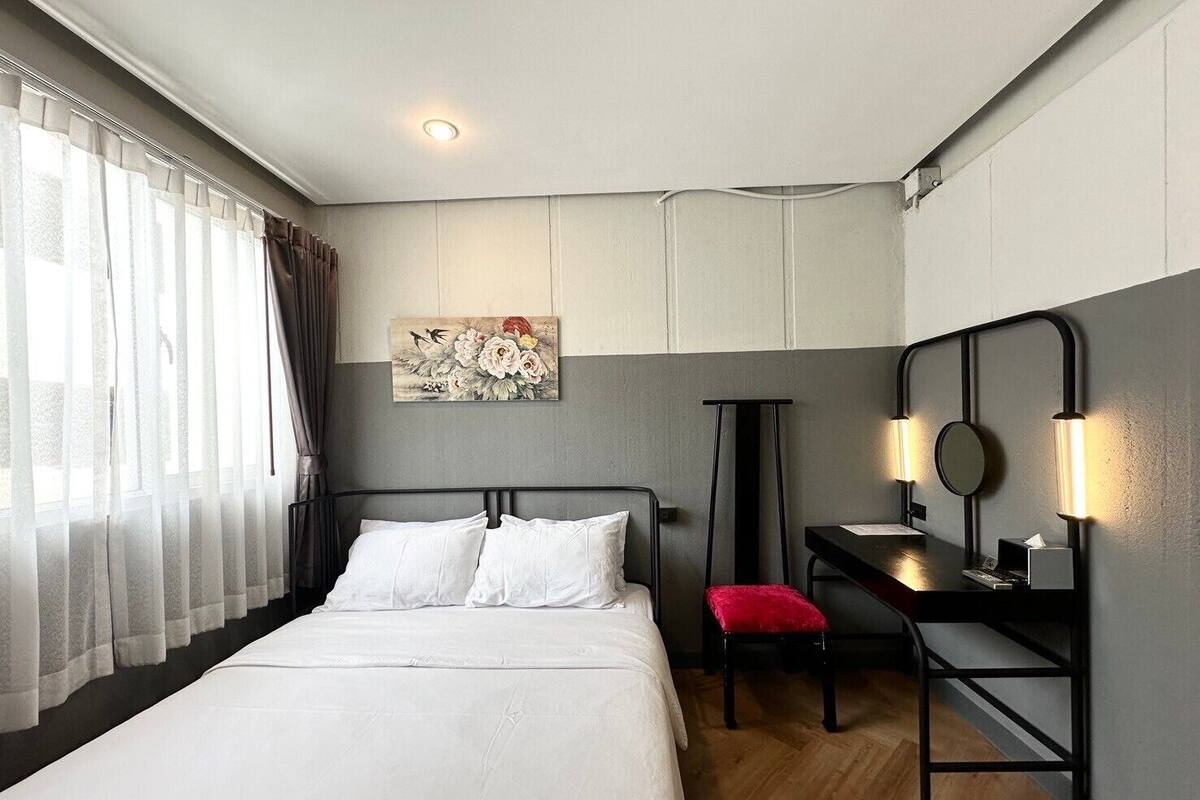 Habitación de hotel con cama, escritorio con silla, espejo y un cuadro en la pared.