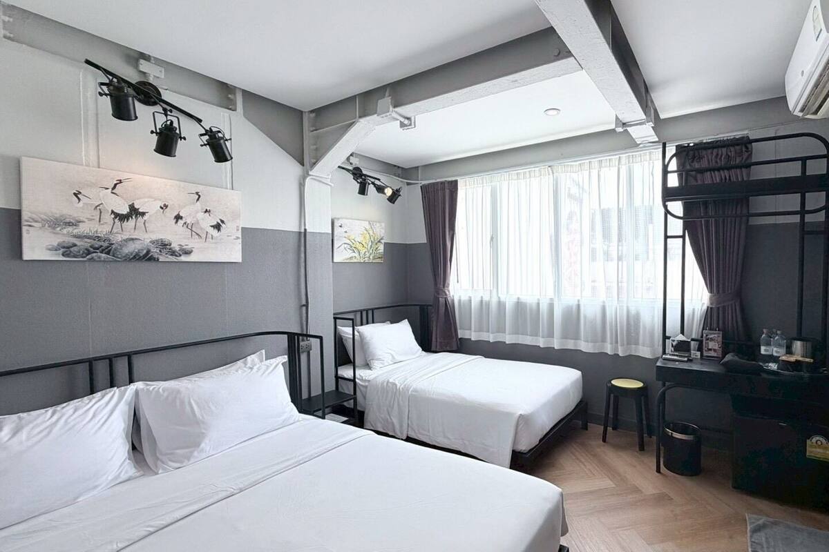 Habitación de hotel con dos camas, un escritorio, una cama nido, una ventana con cortinas y un equipo de aire acondicionado.