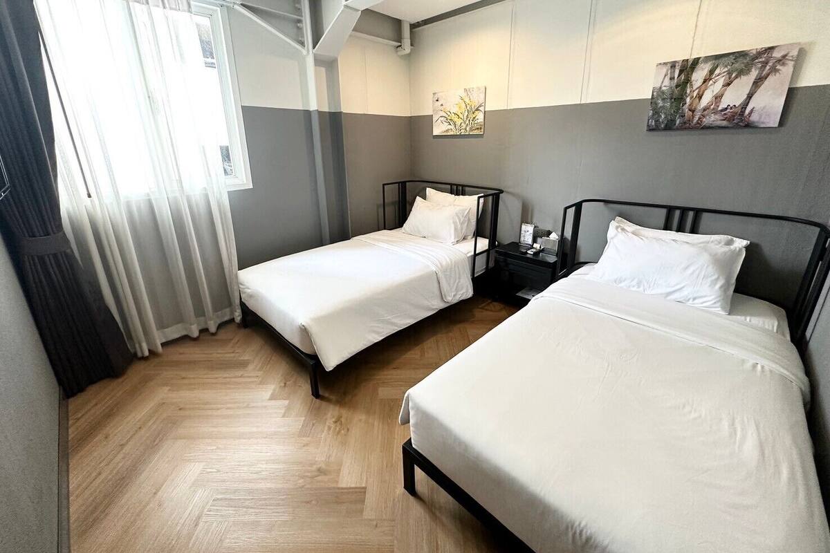 Una habitación de hotel con dos camas, piso de madera, una ventana con cortinas y un cuadro en la pared.