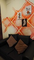Un sofá negro con dos cojines marrones y una pared con arte abstracto y patrones geométricos.