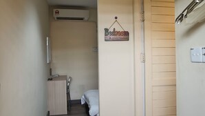 Un couloir étroit, doté d’un plancher en bois, mène à une chambre. Une pancarte sur le mur indique : « Chambre ».