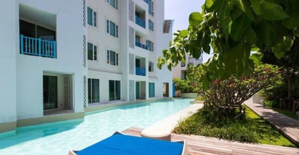 A modern hotel with a swimming pool, balconies, and lush greenery.