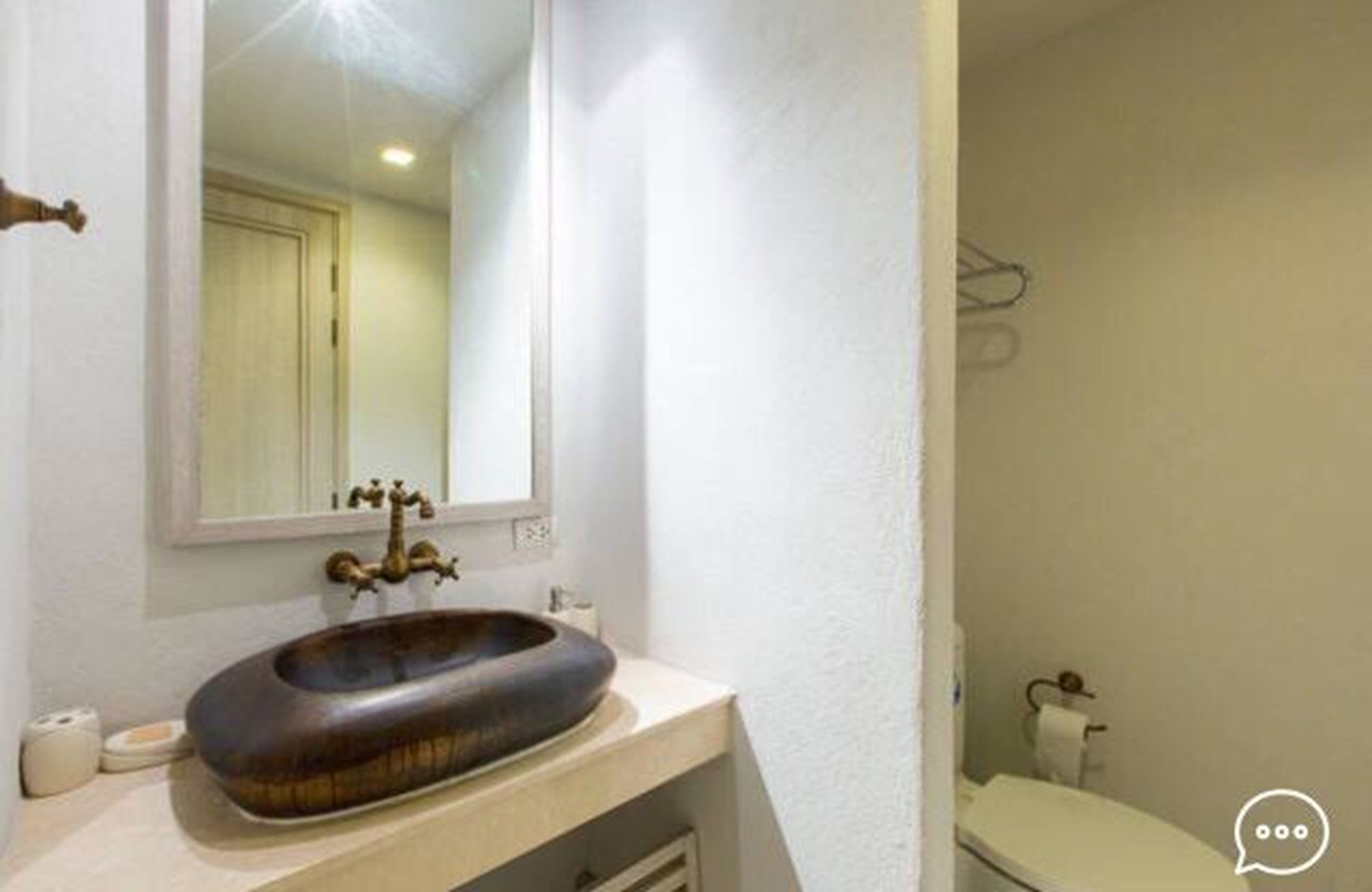 A bathroom with a wooden basin sink, a mirror, and a toilet.
