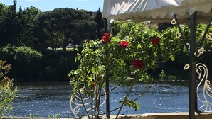 Un gazebo con tettoia bianca affacciato su uno specchio d'acqua, circondato da vegetazione e un percorso in cemento.