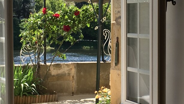 Una finestra con vista su un giardino, un ombrellone bianco e un vaso sul davanzale.