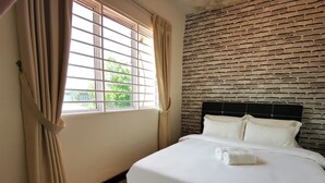Une chambre d’hôtel avec une tête de lit décorée d’un motif en briques, une grande fenêtre avec des rideaux et un lit soigneusement fait, avec une serviette roulée posée dessus.