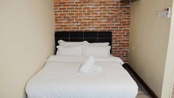 Una cama bien tendida con sábanas y almohadas blancas, cabecera negra y pared con diseño de ladrillo al fondo.
