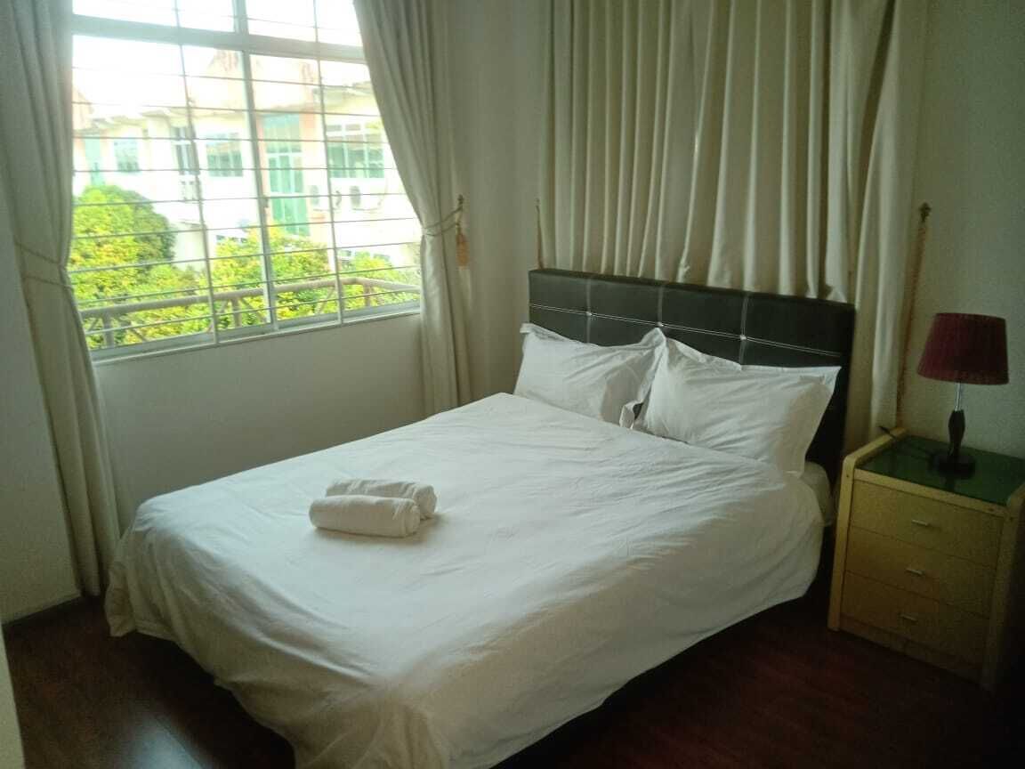 A neatly made bed with white linens and a folded towel, a bedside table with a lamp, and a window with curtains.