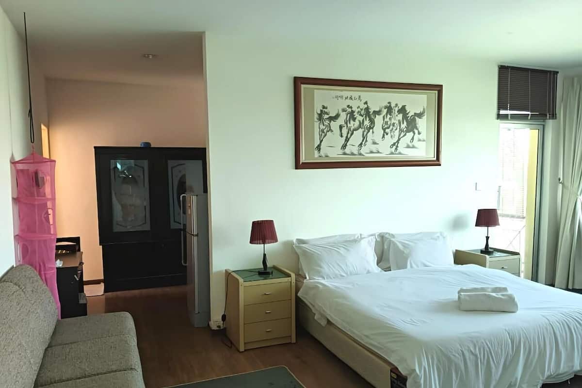 A hotel room with a bed, two bedside tables with lamps, a sofa, a desk, and a wardrobe.