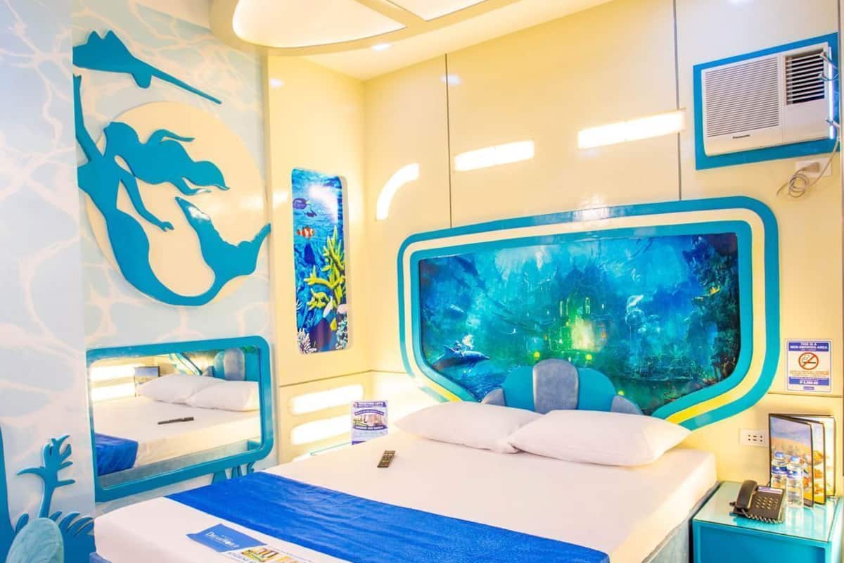 A modern hotel room with a large bed, a wall aquarium, and a ceiling light fixture.