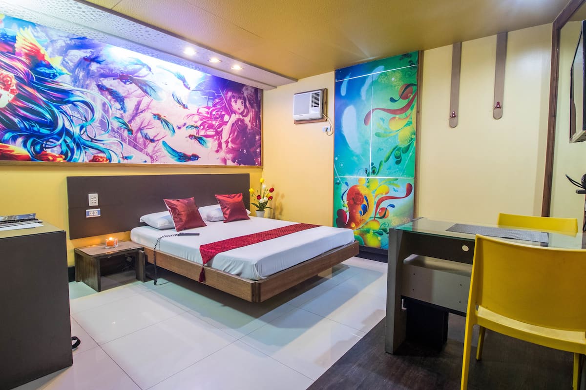 A modern hotel room with a large bed, a desk, and a vibrant abstract mural on the wall.