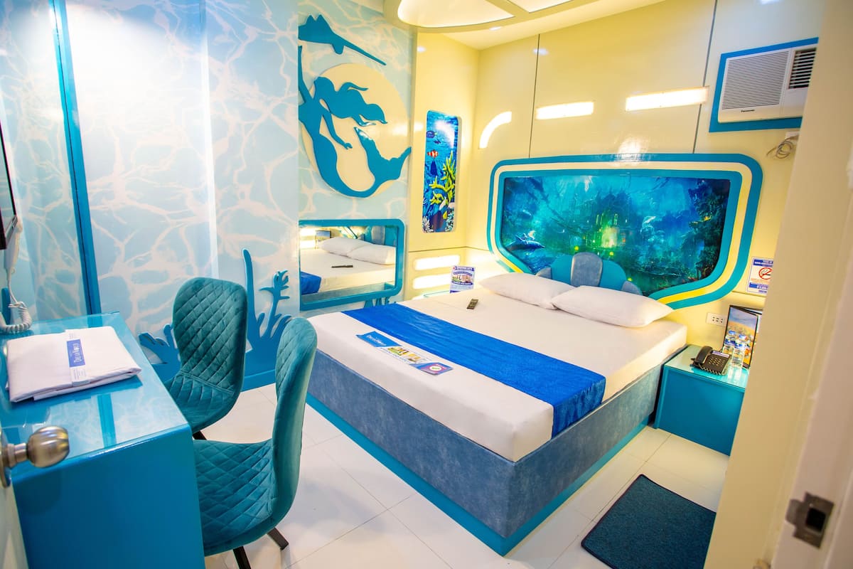 A room with a bed, a desk, a chair, and a large aquarium.