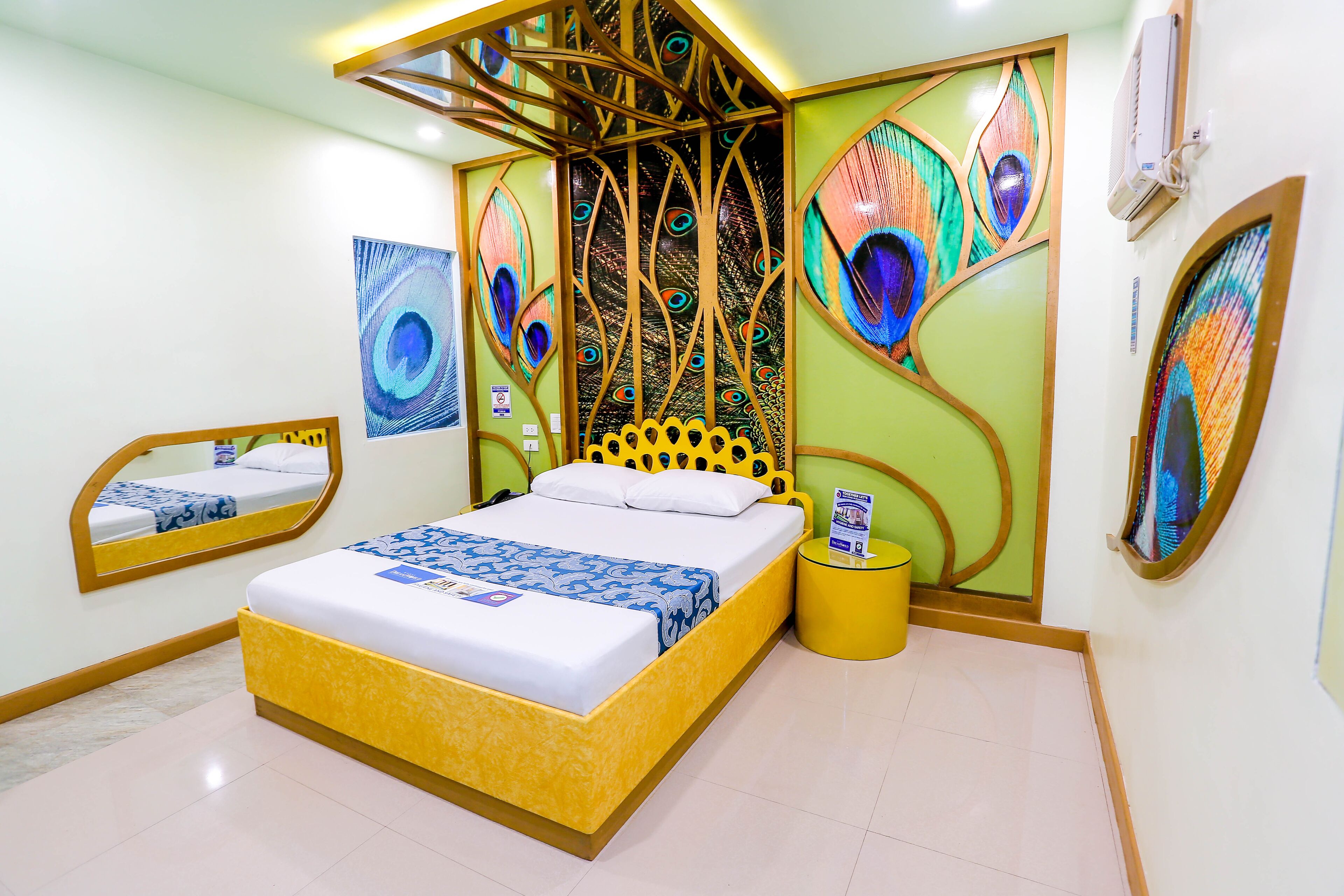 Une chambre à coucher comprenant un lit, un miroir, une table de chevet et des œuvres d’art décoratives sur les murs, le tout sur le thème du paon.