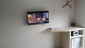 Un televisor de pantalla plana montado en la pared, un perchero de madera, una pequeña planta en maceta y un lavavajillas GE en una zona de cocina.