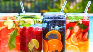 Cuatro frascos de vidrio con fruta y menta, cada uno con una pajita, junto a una piscina.