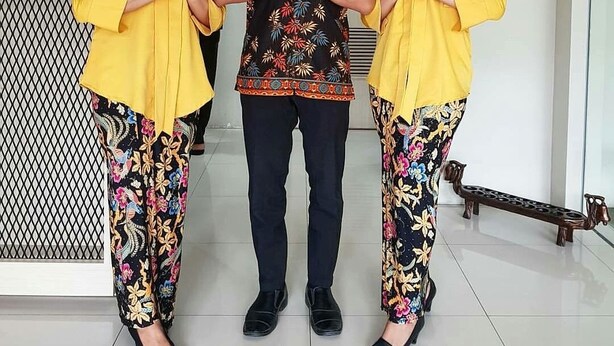 Tres personas en una zona de recepción de diseño moderno, que incluye un mostrador de recepción y un arreglo floral azul decorativo.