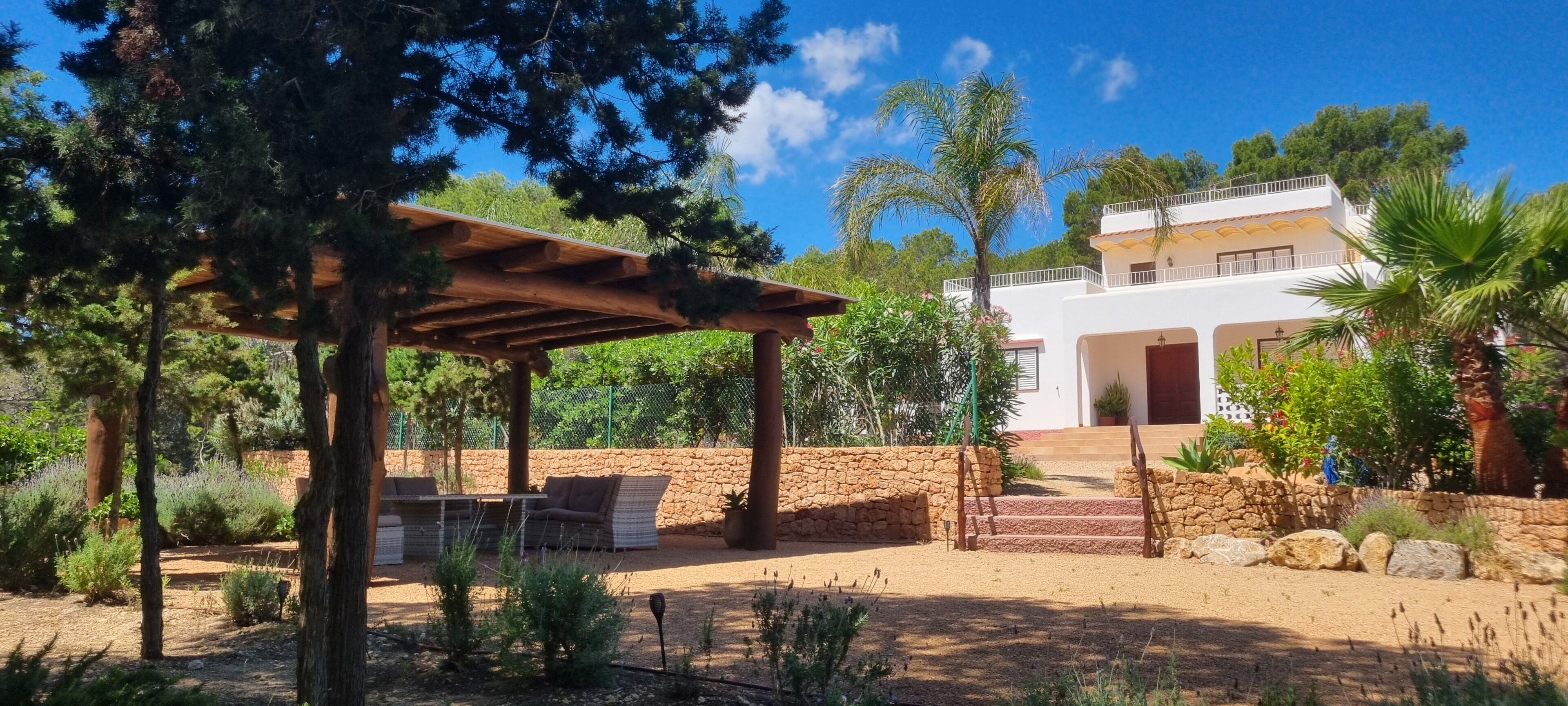 Una casa moderna con patio de piedra, mobiliario exterior y una pérgola de madera.