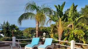 A poolside area with two lounge chairs, a tiled pool, and a view of the sea and surrounding greenery. - Villa with pool and barbecue near the beach (Ibiza)