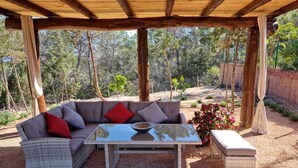 An outdoor seating area with a wooden pergola, a cushioned sofa with red cushions, a glass-top table, and a small side table. - Villa with pool and barbecue near the beach (Ibiza)