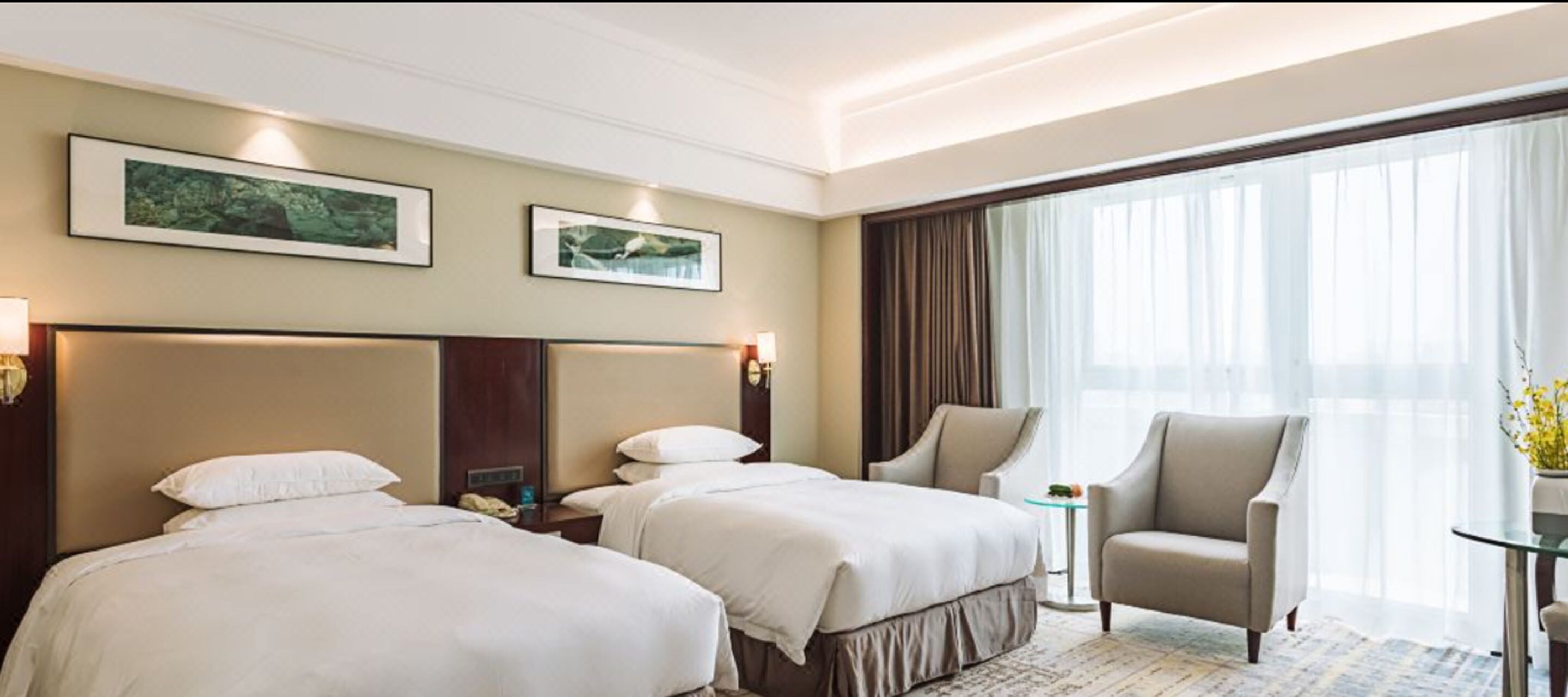 A hotel room with two beds, a chair, a small table, and a large window with curtains.