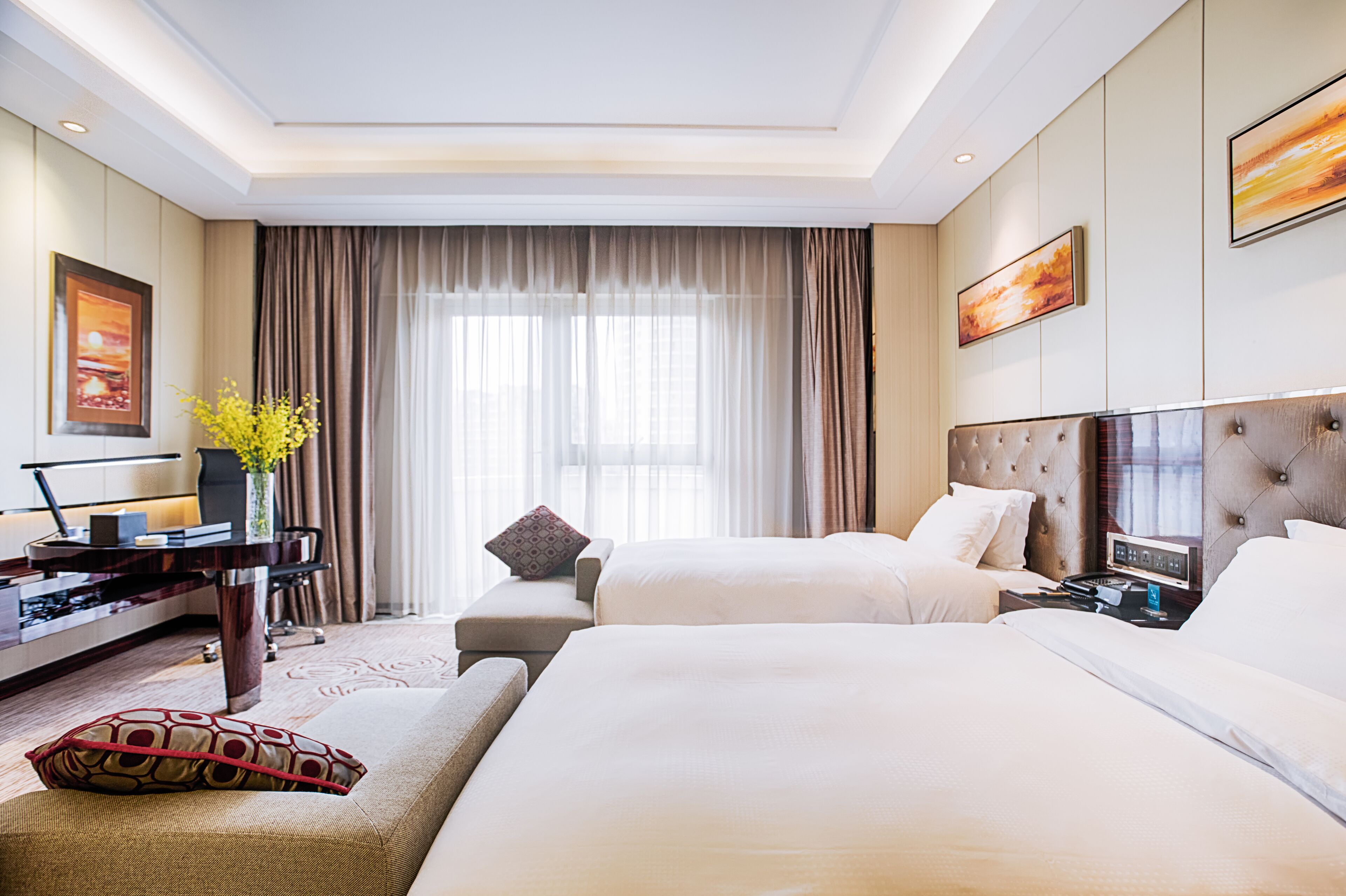 A hotel room with two beds, a desk, a chair, and a large window with curtains.