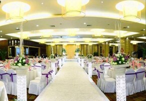 A banquet hall with a central aisle, white tables with purple sashes, and floral centerpieces.