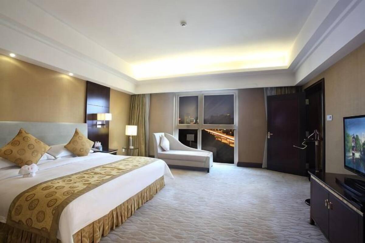 A hotel room with a large bed, a sofa, a television, and a window with a city view.