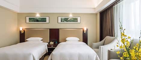 A hotel room with two beds, a desk, and a chair. There are two framed pictures on the wall above the beds.