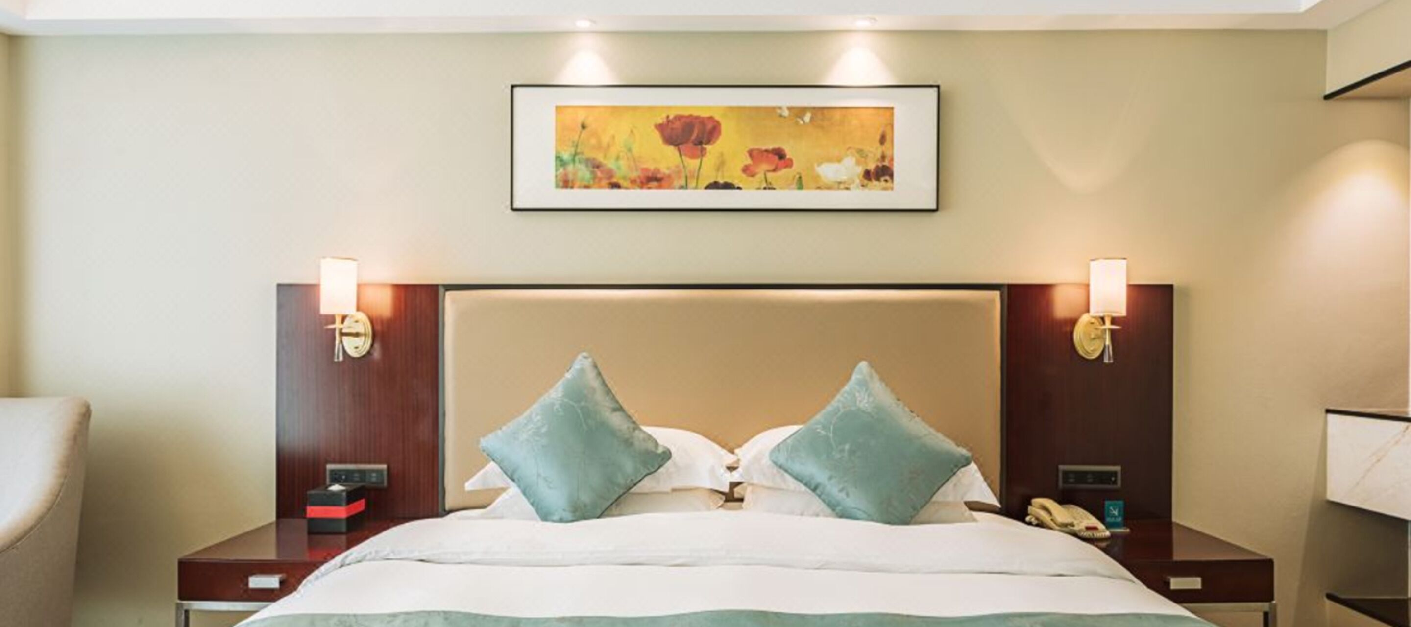 Een hotelkamer met een groot bed, twee nachtkastjes, een schilderij aan de muur en twee wandlampen.