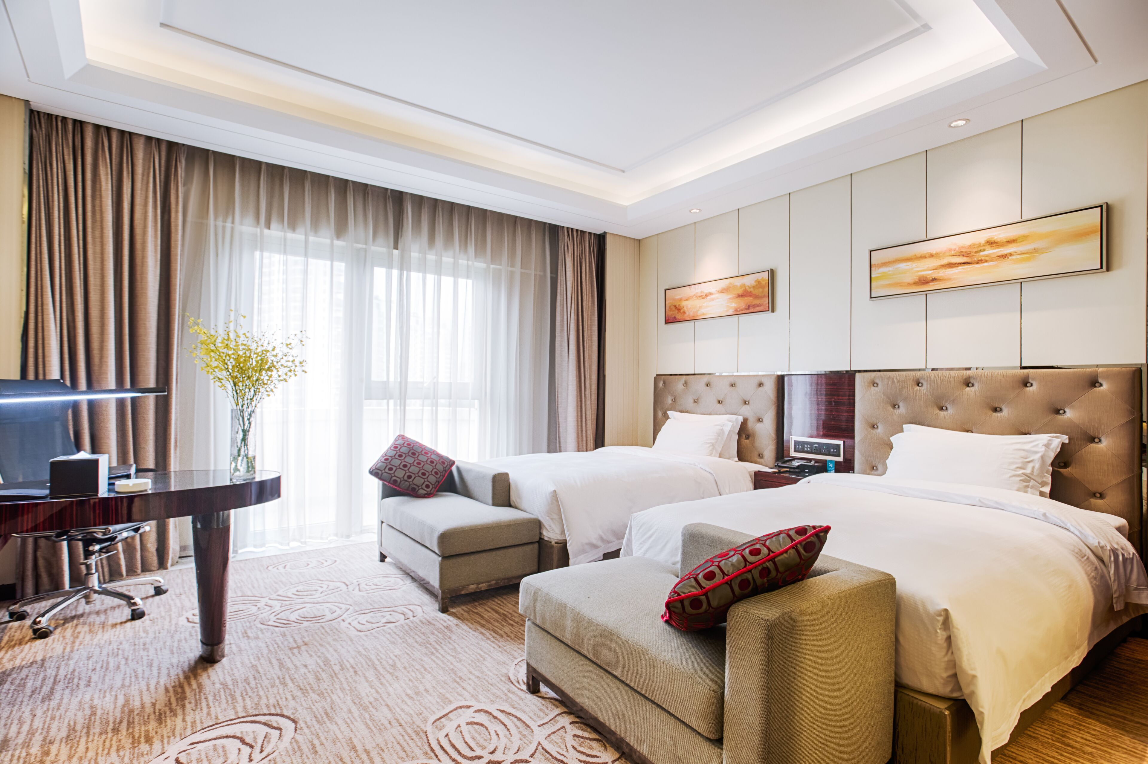 A hotel room with two beds, a desk, a chair, and a large window with curtains.