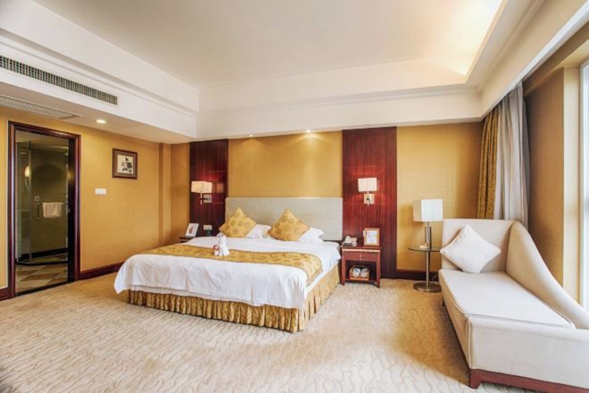 A hotel room with a large bed, a sofa, a desk, and a lamp.