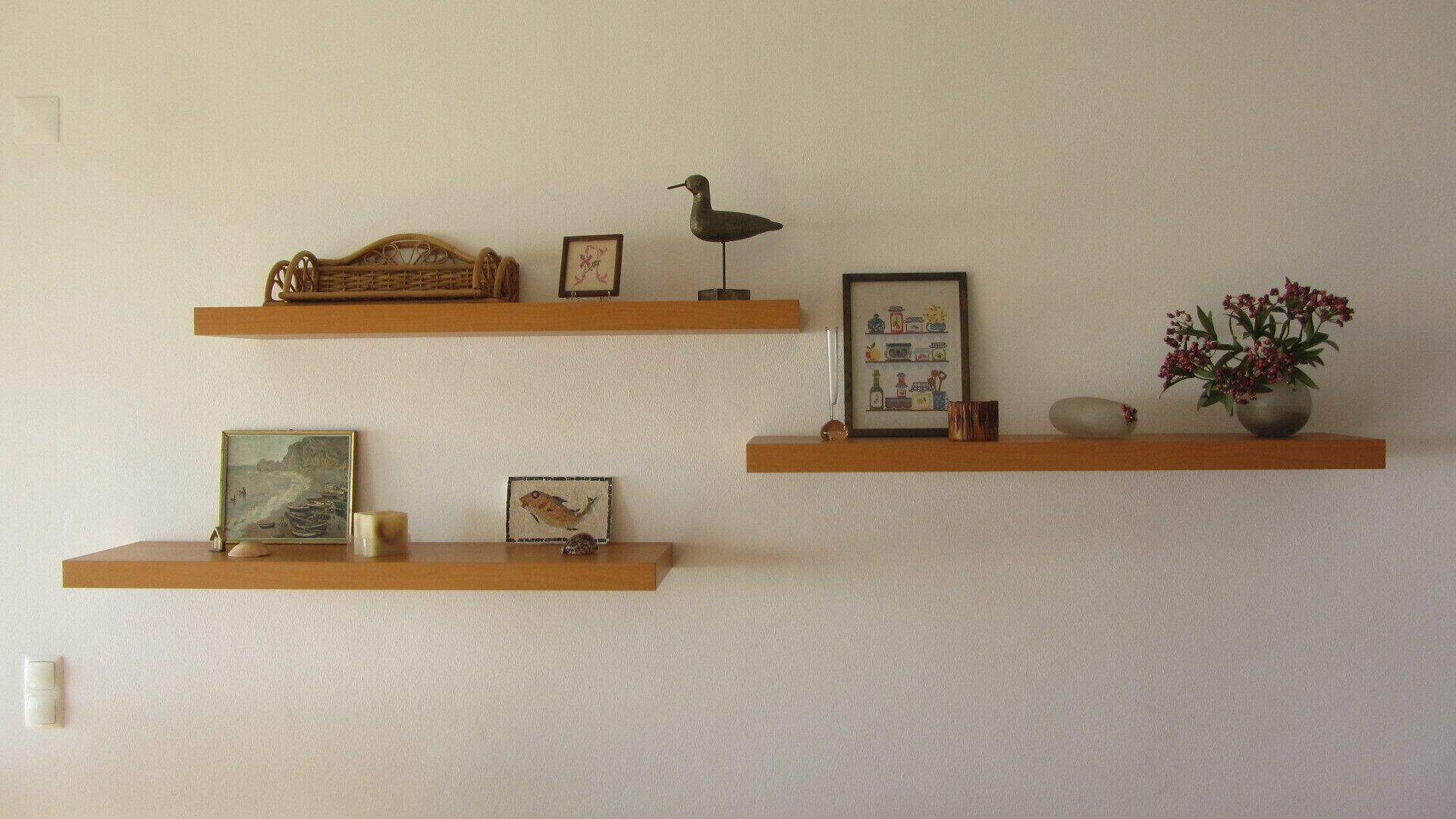 Tres repisas de madera con varios objetos decorativos, incluyendo cuadros enmarcados, una escultura de pájaro y un florero con flores.