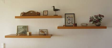 Tres repisas de madera con varios objetos decorativos, incluyendo cuadros enmarcados, una escultura de pájaro y un florero con flores.